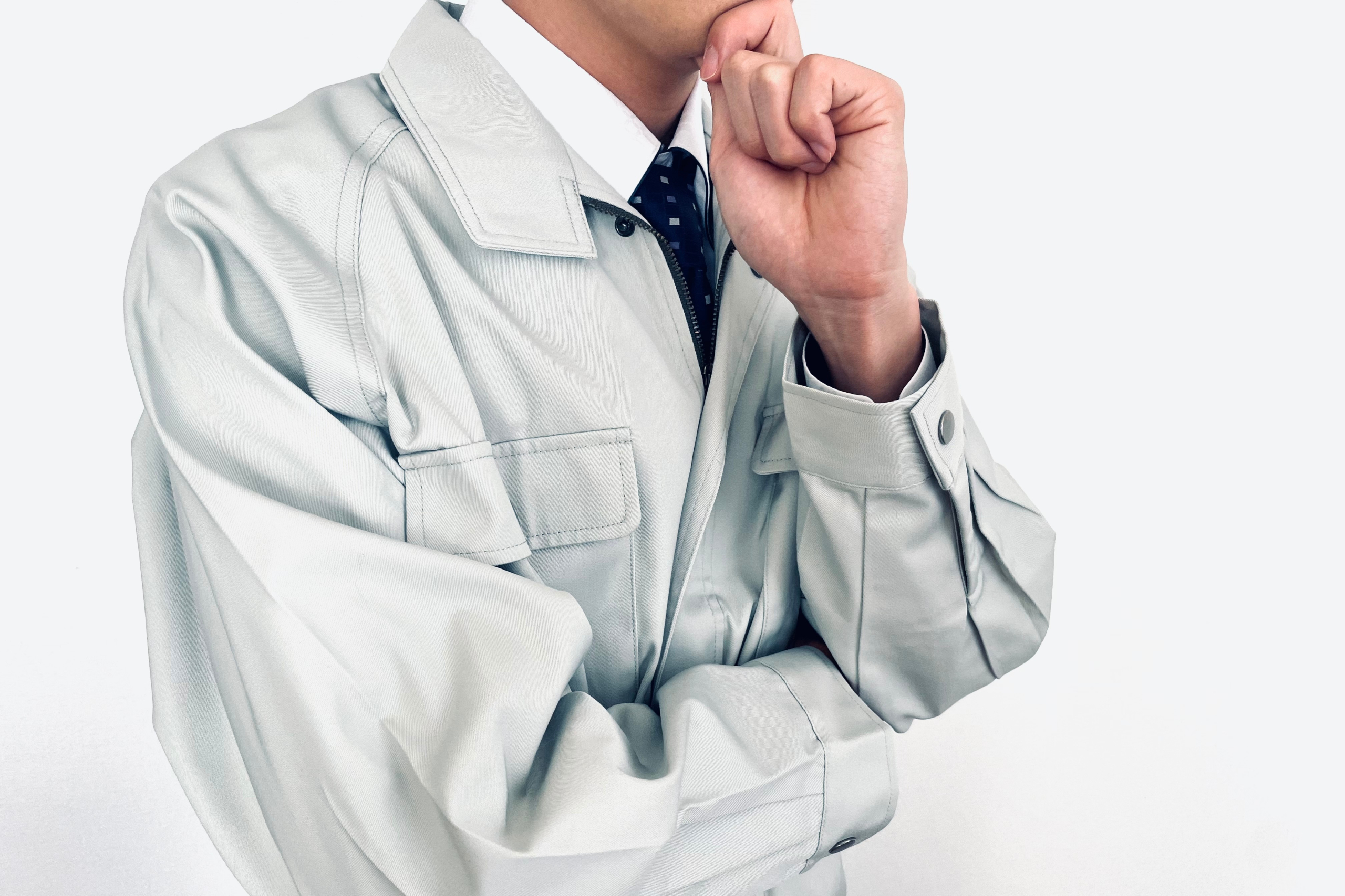作業服を着てネクタイを締めた人物が、腕を組み、手を顎に当てて何かを考えている様子。